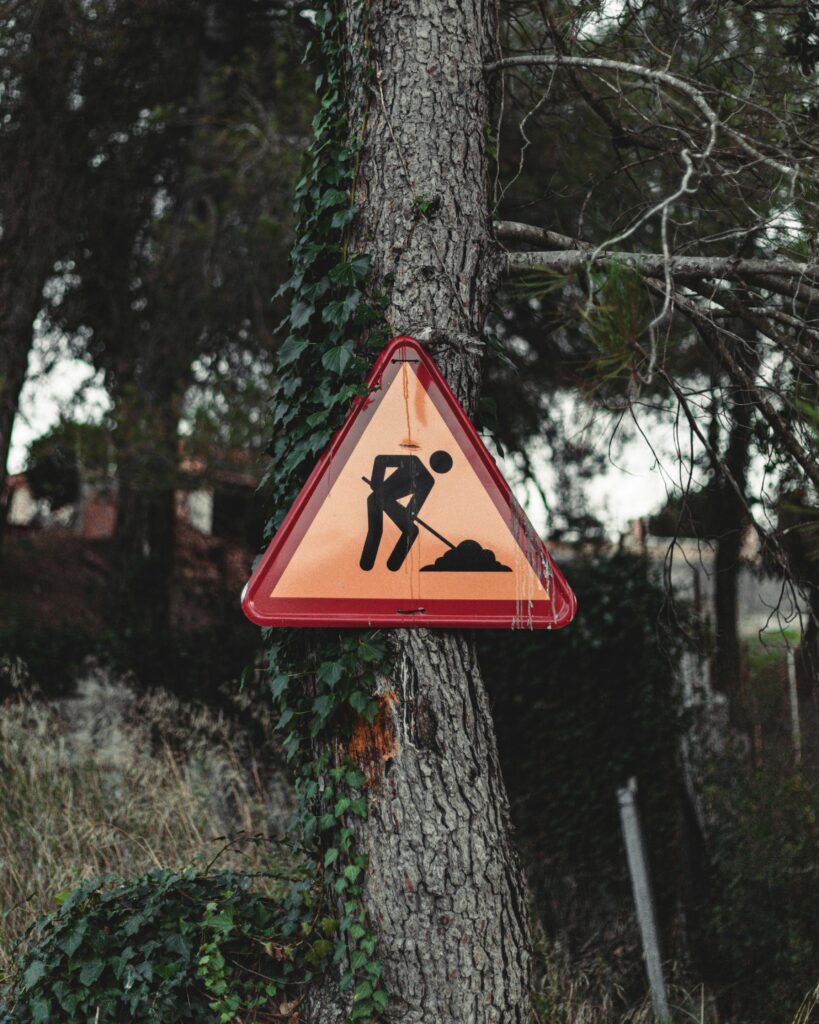 Triangular construction sign on a tree in a forested area of Barcelona.